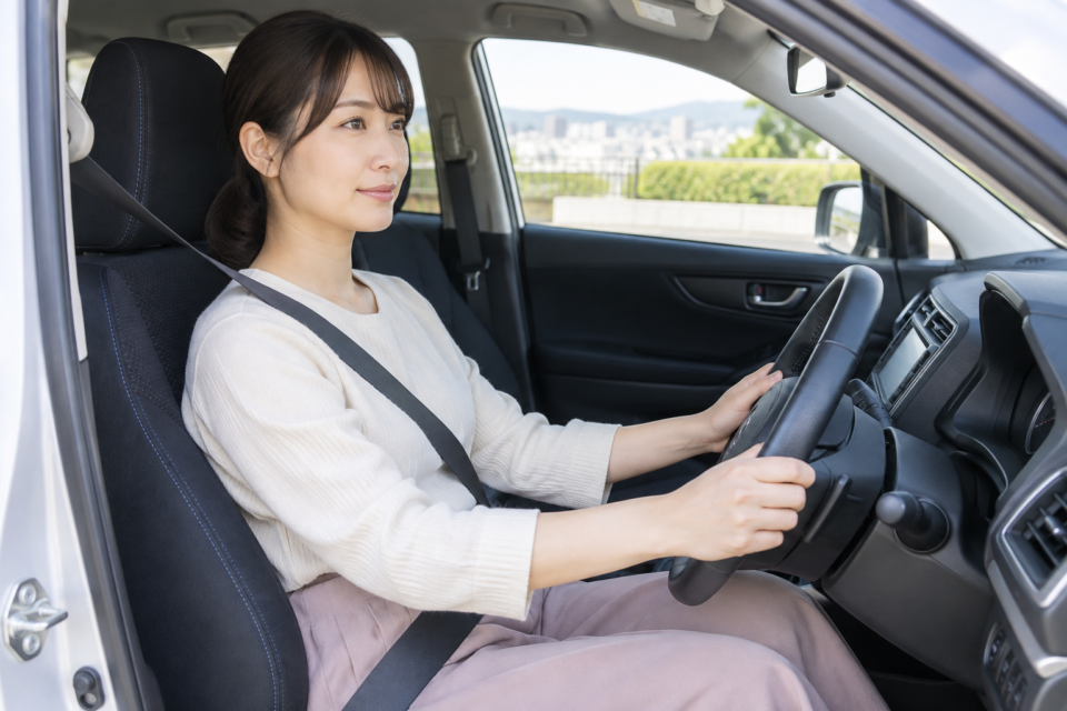 停車中の車内でシートベルトを着用してハンドルに手を添える女性