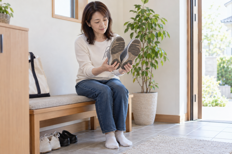 玄関で左右のスニーカーの靴底を見比べる女性